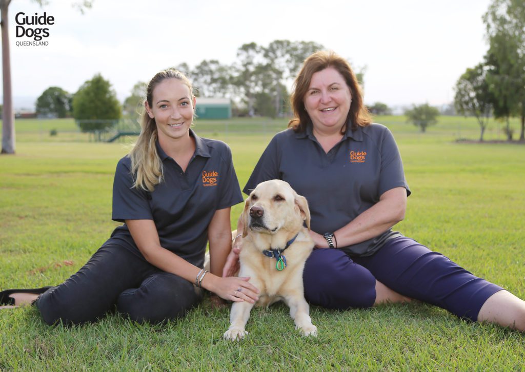 Image of two female Occupational Therapists sitting either side of a yellow Guide Dog