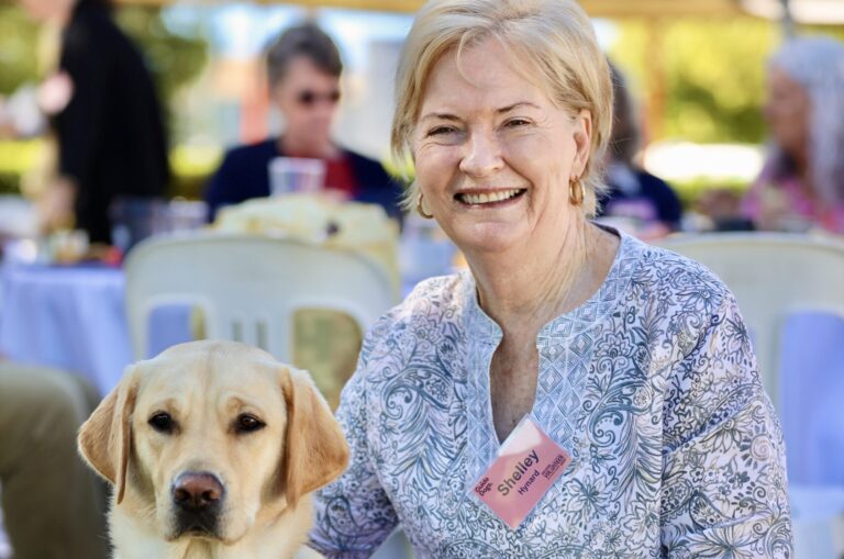 Shelley is smiling at the camera and has her arm around yellow Labrador and Guide Dogs ambassador dog, Vanda.