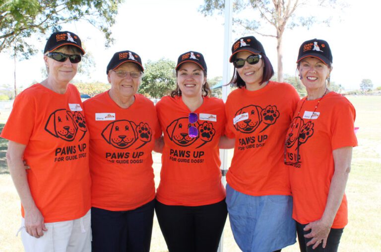 Image of five female volunteers wearing bright orange supporter shirts and standing as a group