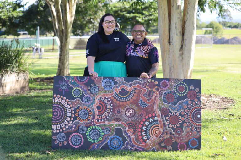 Client Services team member Sarah stands with artist Laurie Anno and the artwork he presented to Guide Dogs Queensland.