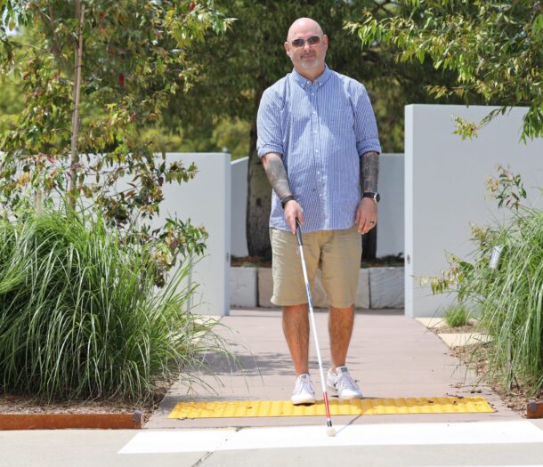 Darren Solly walking across a pedestrian crossing using a white cane