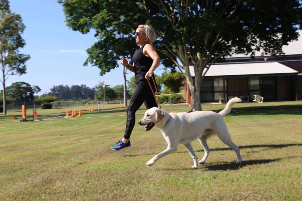 Image of a woman in activewear running with a yellow dog