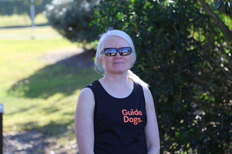 Client Lay is pictured smiling to camera wearing glasses and a Guide Dogs singlet