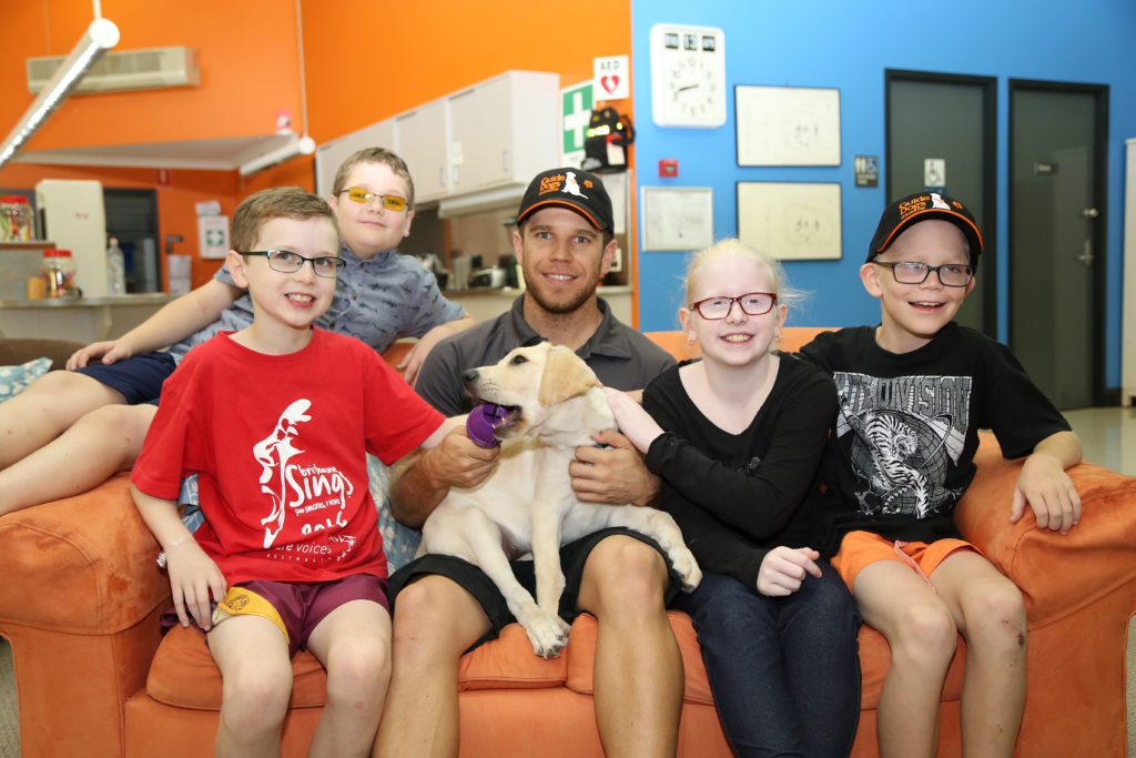 Image of four children sitting on a lounge beside a Guide Dog Trainer and a yellow Guide Dog puppy