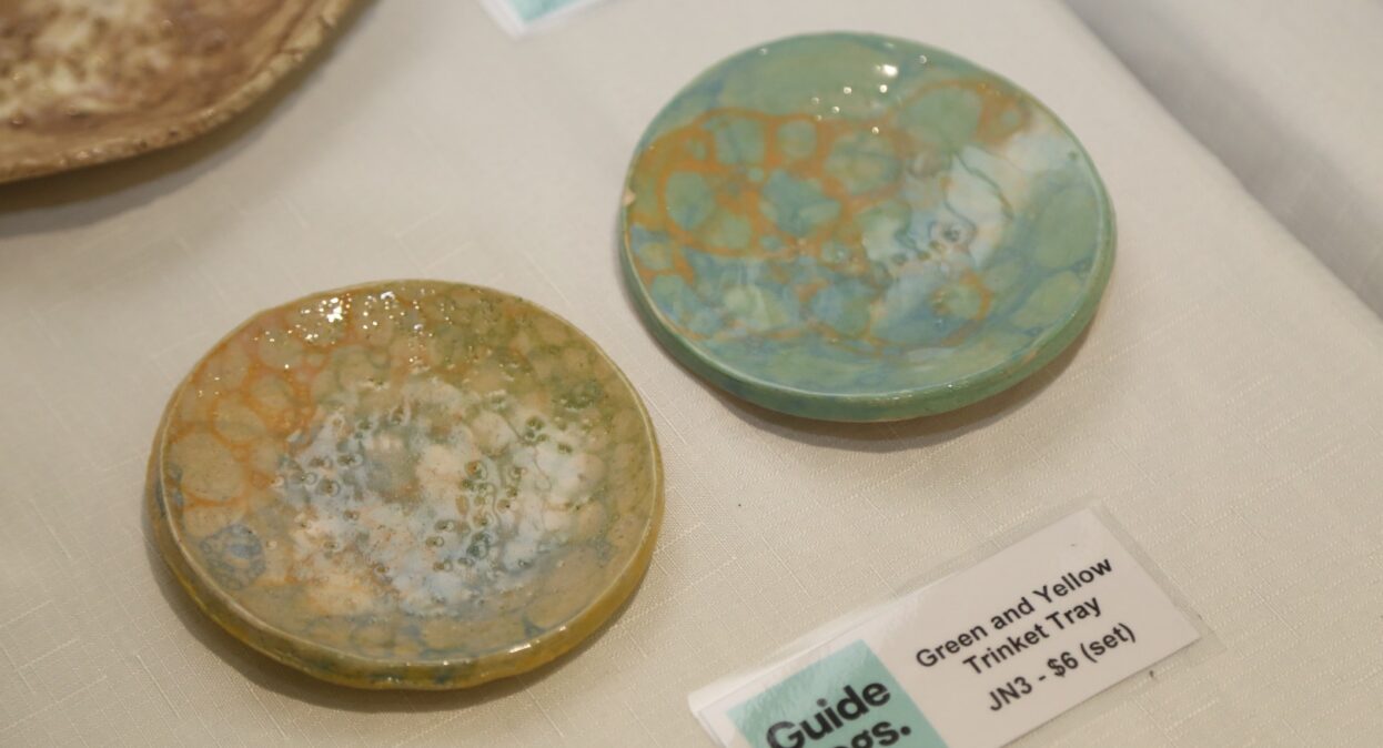 Two small, round ceramic trinket trays with glazed green, yellow, and blue bubble-like patterns sit next to a "Guide Dogs" price label.