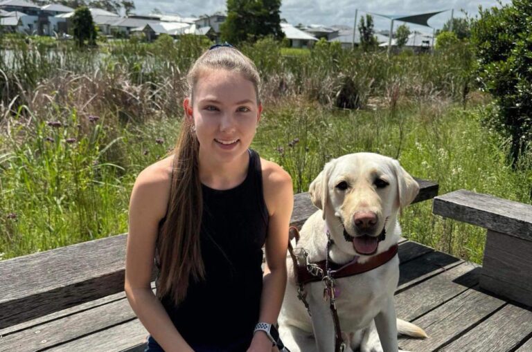 Karlee sits next to her yellow Guide Dog in harness