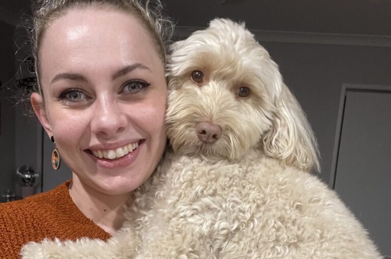 Lauren is pictured smiling to camera while holding golden labradoodle Dolly.