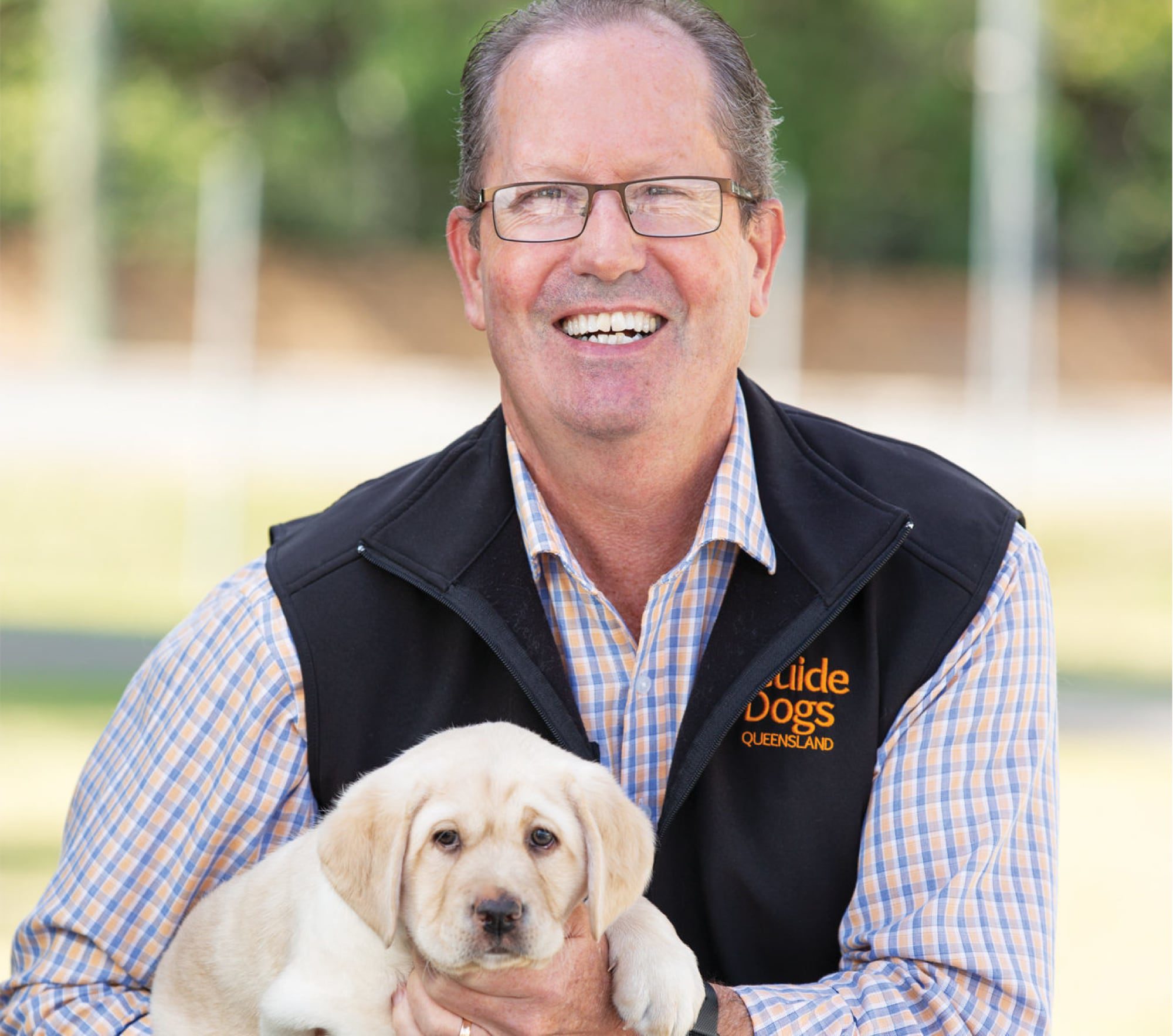Guide Dogs Queensland Chief Executive Officer, Michael Green. Michael is holding an eight week old yellow labrador puppy and they are both looking at the camera. Michael is smiling.