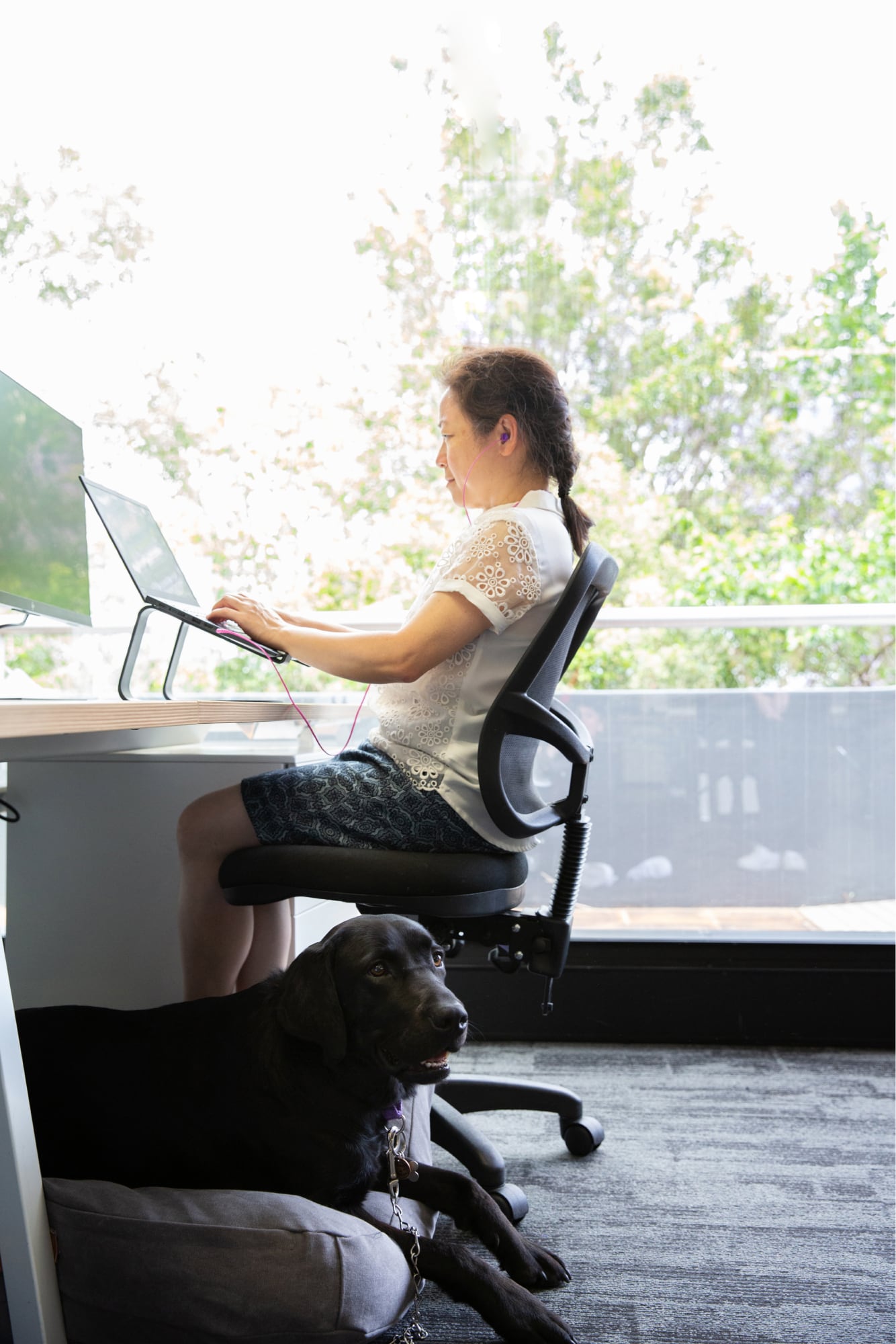 A person sitting at a desk using their laptop. The image is a profile view.