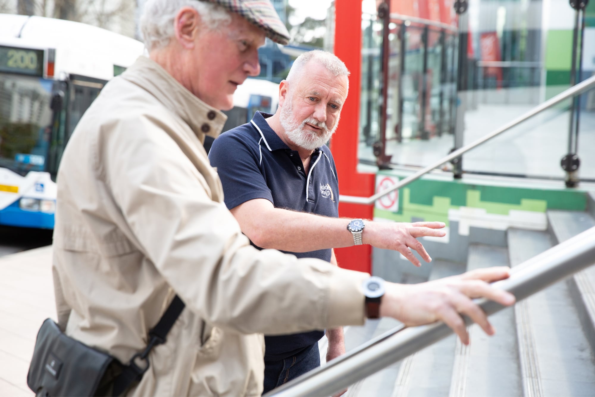 A Guide Dogs staff member assisting an an older adult with navigating a handrail.