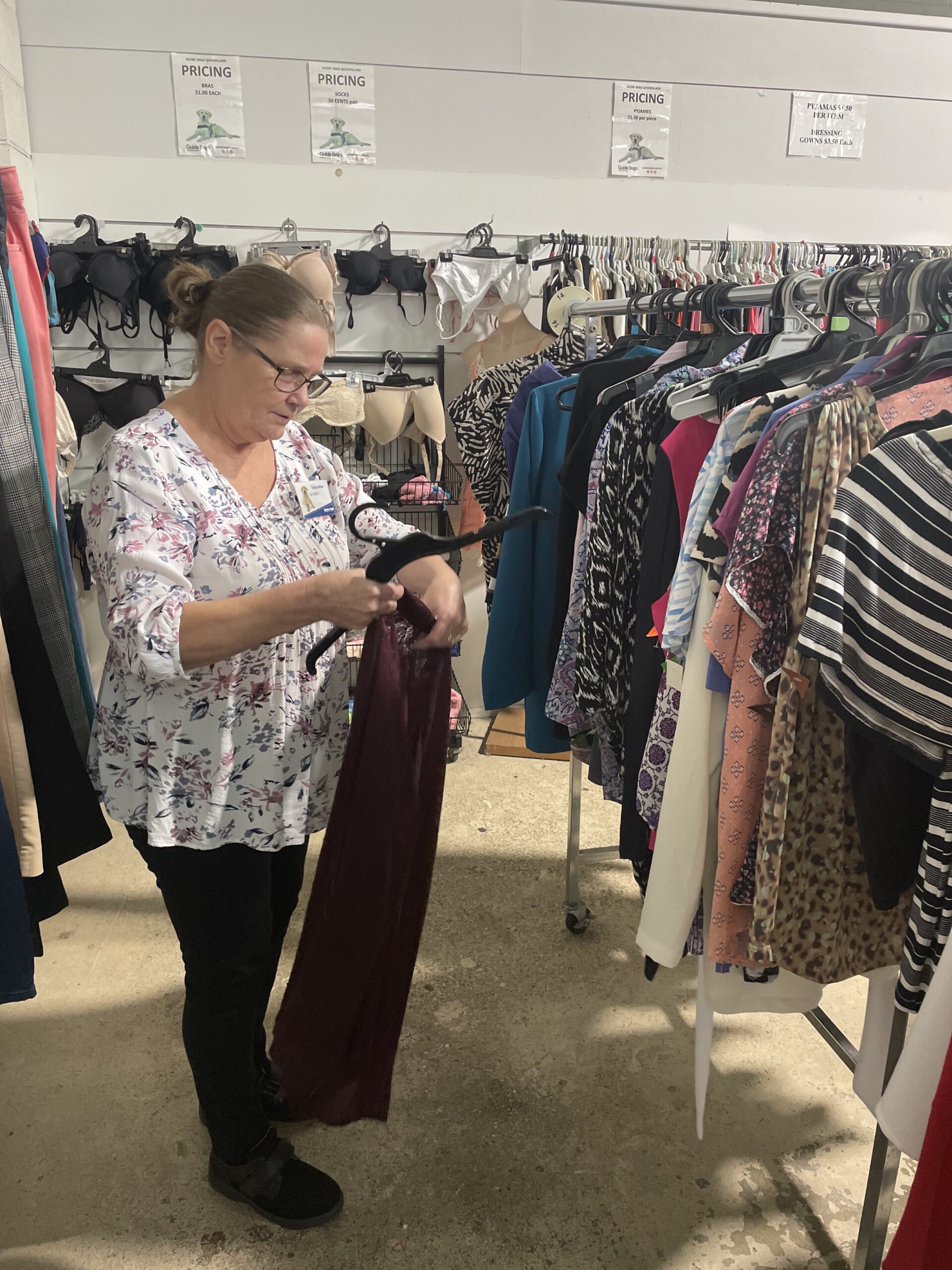 a woman hanging up a dress on an op shop clothing rack.