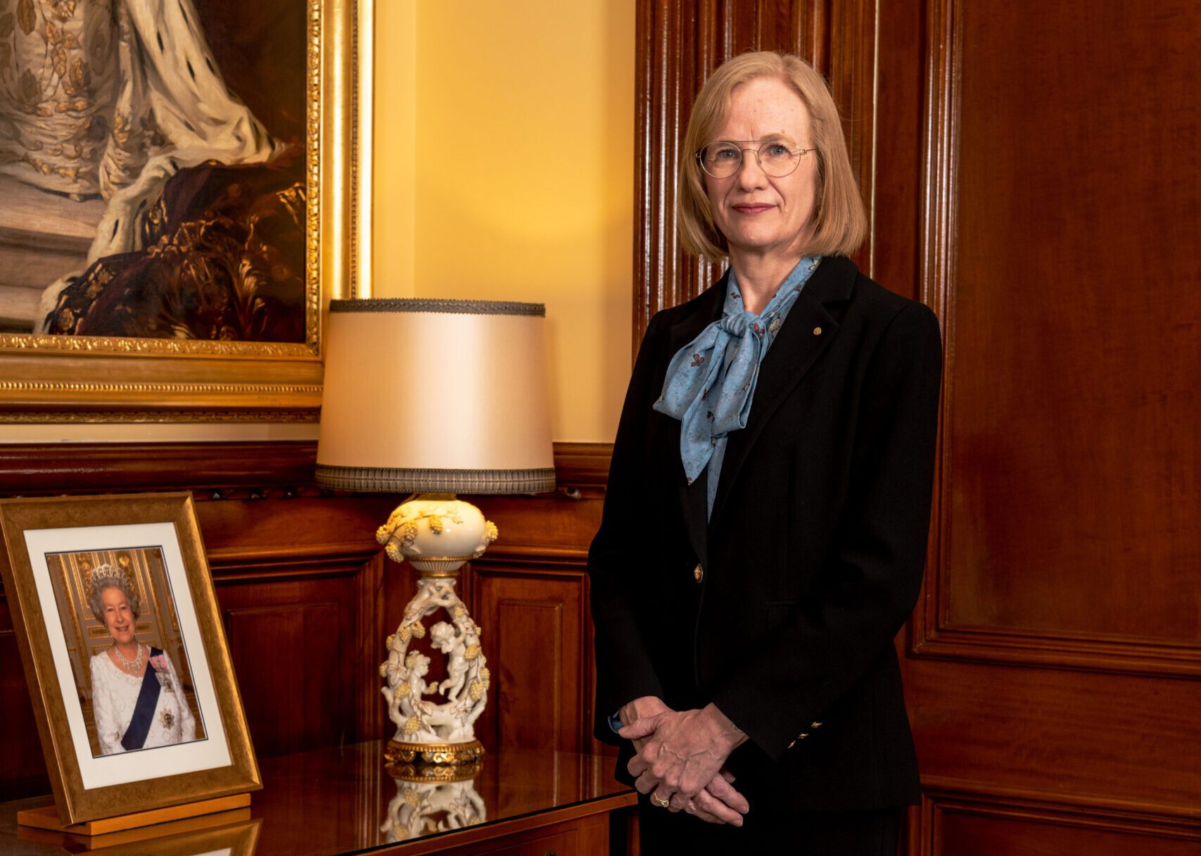 Her Excellency the Honourable Dr Jeannette Young PSM Governor of Queensland standing next to a side table with a framed photo of Her Majesty Queen Elizabeth II