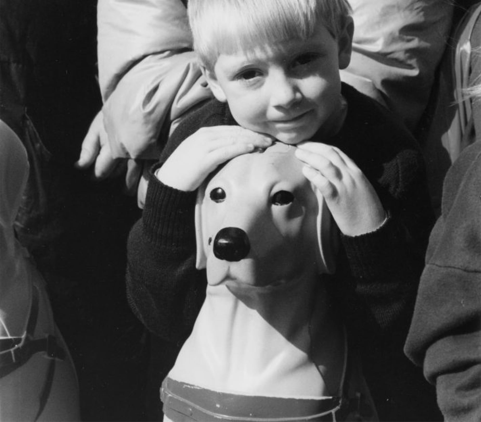 A black and white photo of a young child leaning against a vintage Guide Dogs collection dog.
