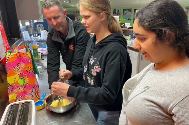Occupational Therapist, Justin, is pictured working with two students using a whisk in the Guide Dogs kitchen.