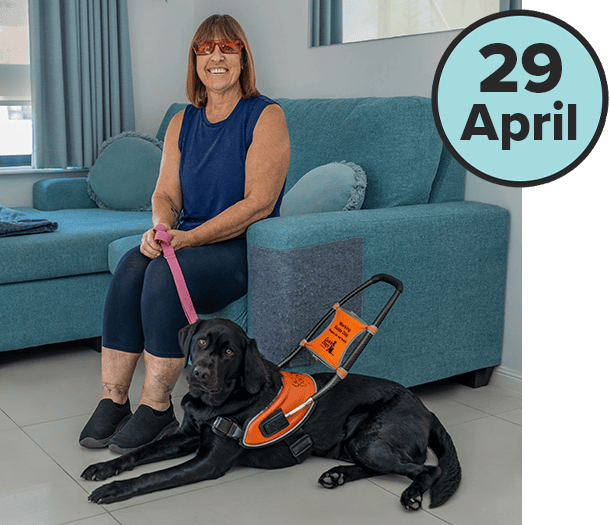 Image shows a woman sitting on a chair next to a black Guide Dog in an orange harness. Black text in a blue circle reads '29 April' for International Guide Dog Day 2026.