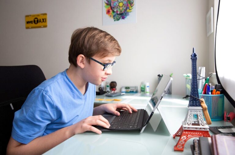 A teenage boy with glasses is pictured sitting down and looking at a laptop.