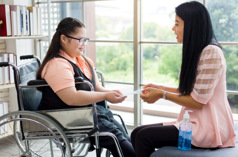 A psychologist is pictured holding out a card to young girl wearing glasses in a wheelchair.