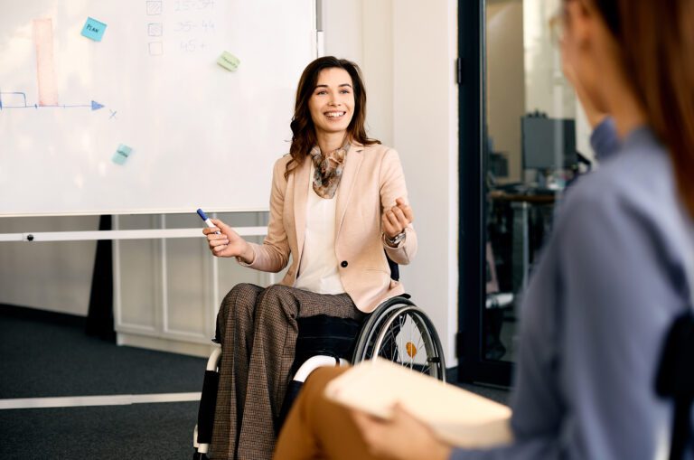 A business woman in a wheelchair is pictured presenting in front of a whiteboard