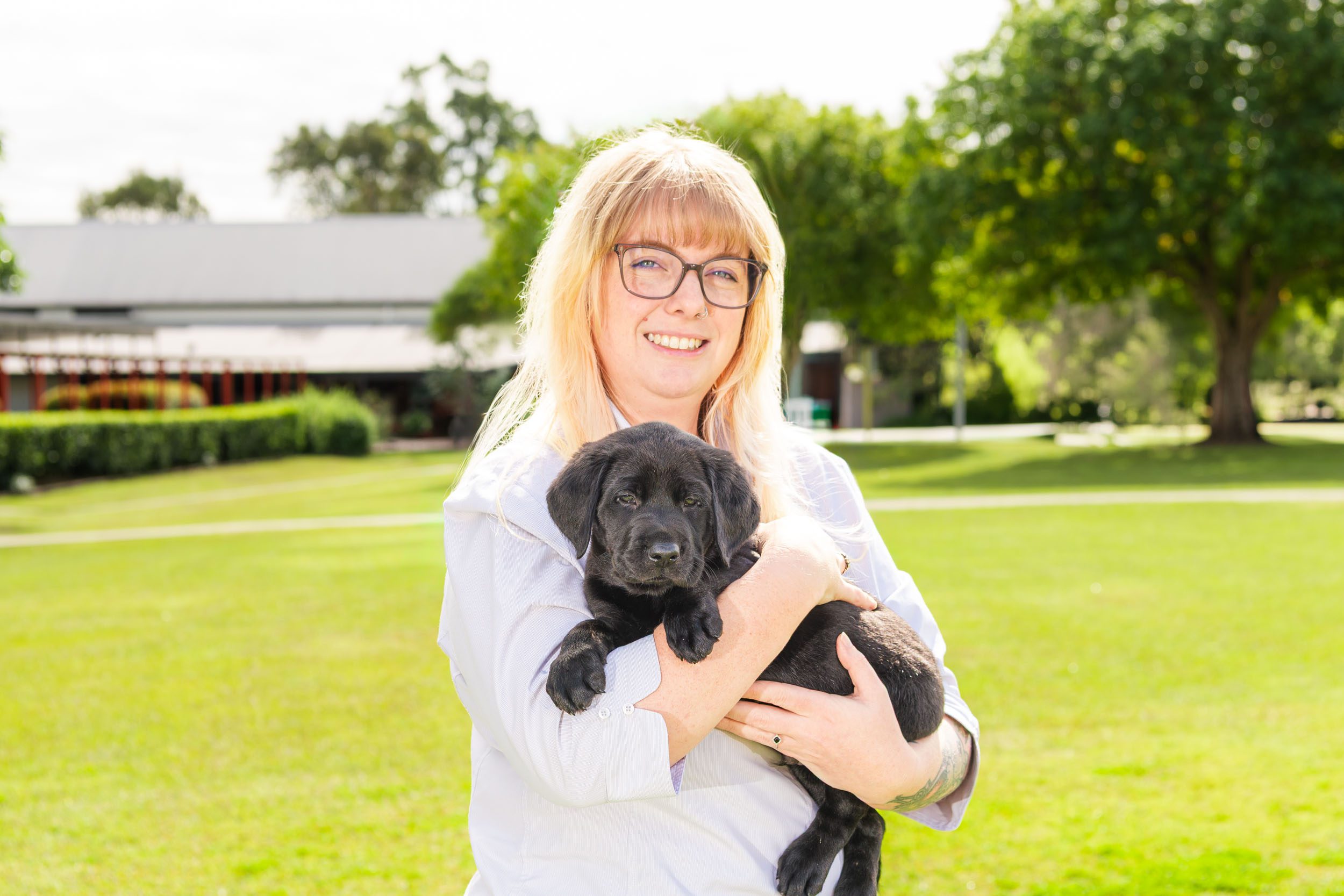 A headshot image of Guide Dogs Queensland psychologist Rebekah holding a black labrador puppy and smiling at the camera.