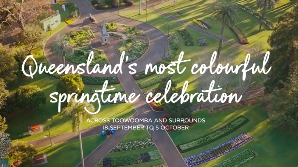An aerial view of a park featuring vibrant, geometric flower beds and walking paths, overlaid with the text "Queensland's most colourful springtime celebration."