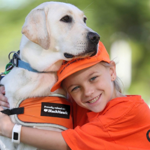 Young fundraiser hugging a Guide Dog while wearing orange.