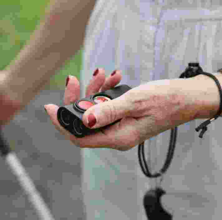 Person standing outside with a white cane in one hand and a Miniguide in the other.