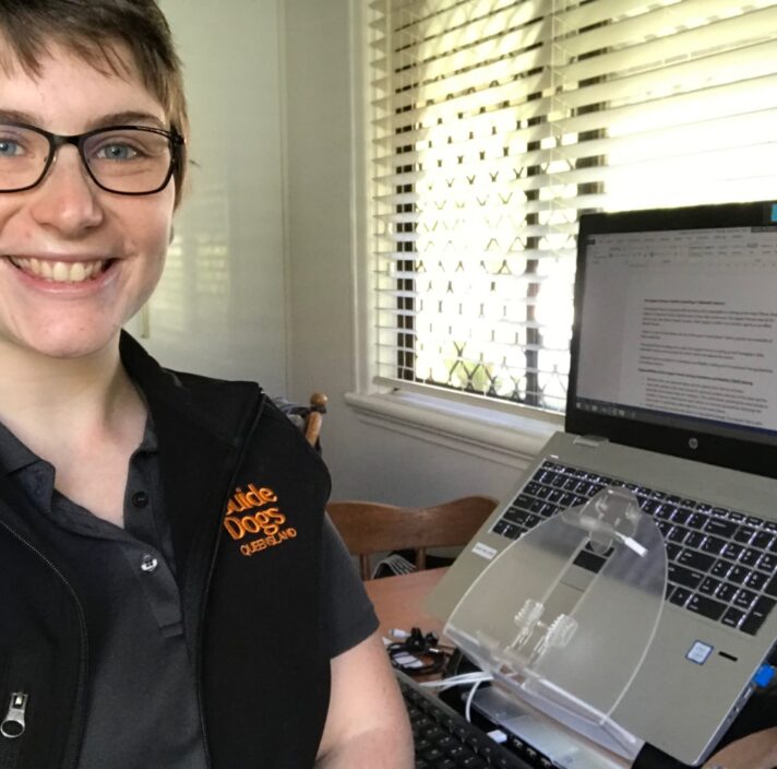A Guide Dog's staff member sitting at a laptop. The staff member is looking at the camera smiling