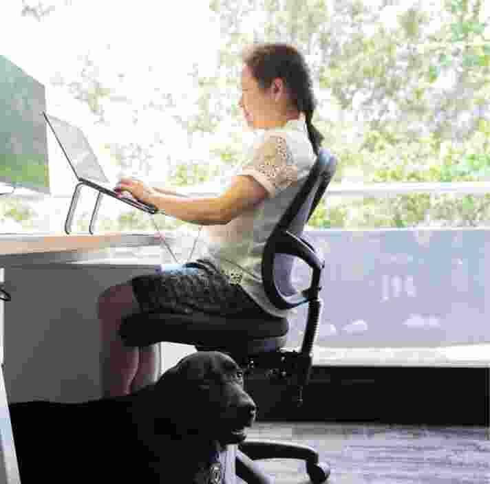 A person sitting at a desk using their laptop. The image is a profile view.