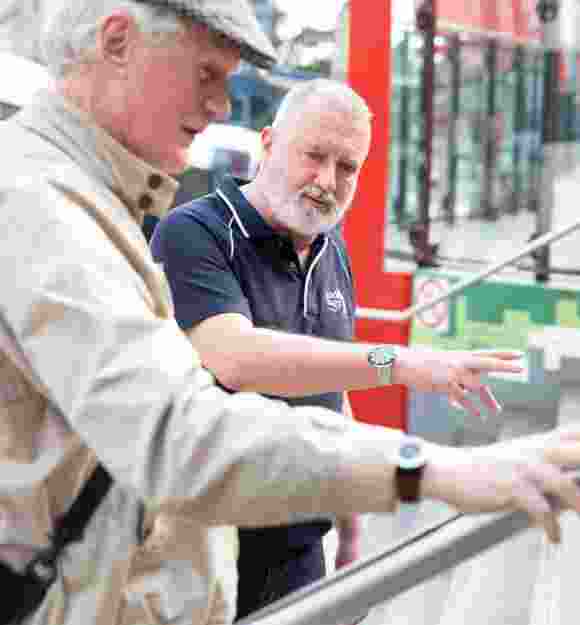A Guide Dogs staff member assisting an an older adult with navigating a handrail.
