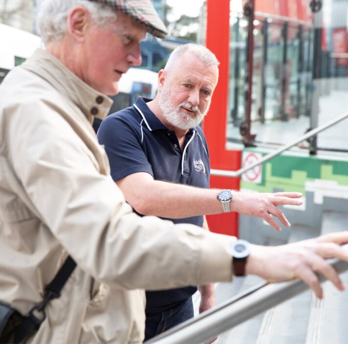 A Guide Dogs staff member assisting an an older adult with navigating a handrail.