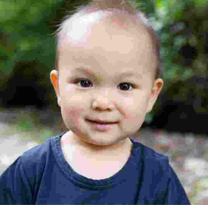 A young baby looking at the camera with a small smile on their face.