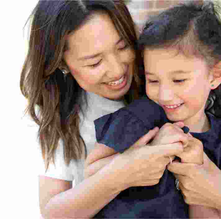 A mother and young child embrace. The mother is cuddling her child from behind.